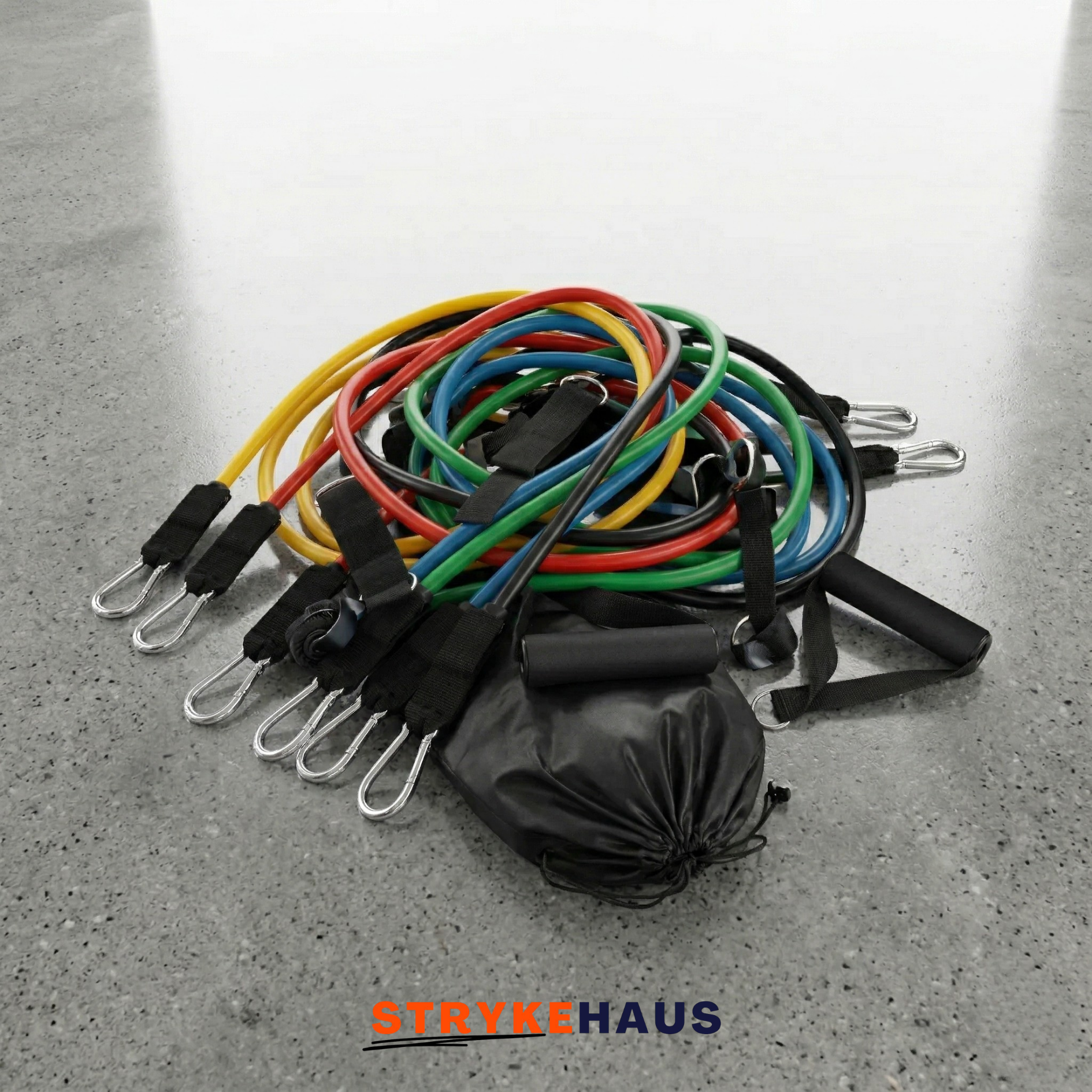 Set of colorful resistance bands with a black drawstring bag on a gray concrete floor, featuring the brand 'StrykeHaus'.